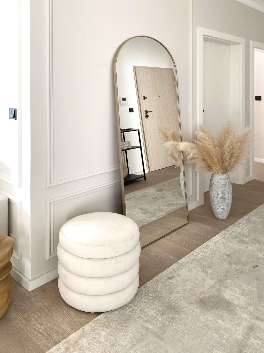 duże lustro arkadowe w złotej ramie oparte o ścianę w beżowym korytarzu