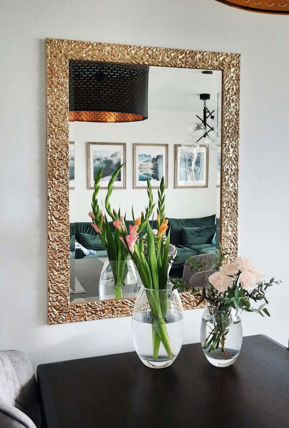 lustro w złotej zdobionej ramie w salonie powieszone nad czarnym stołem