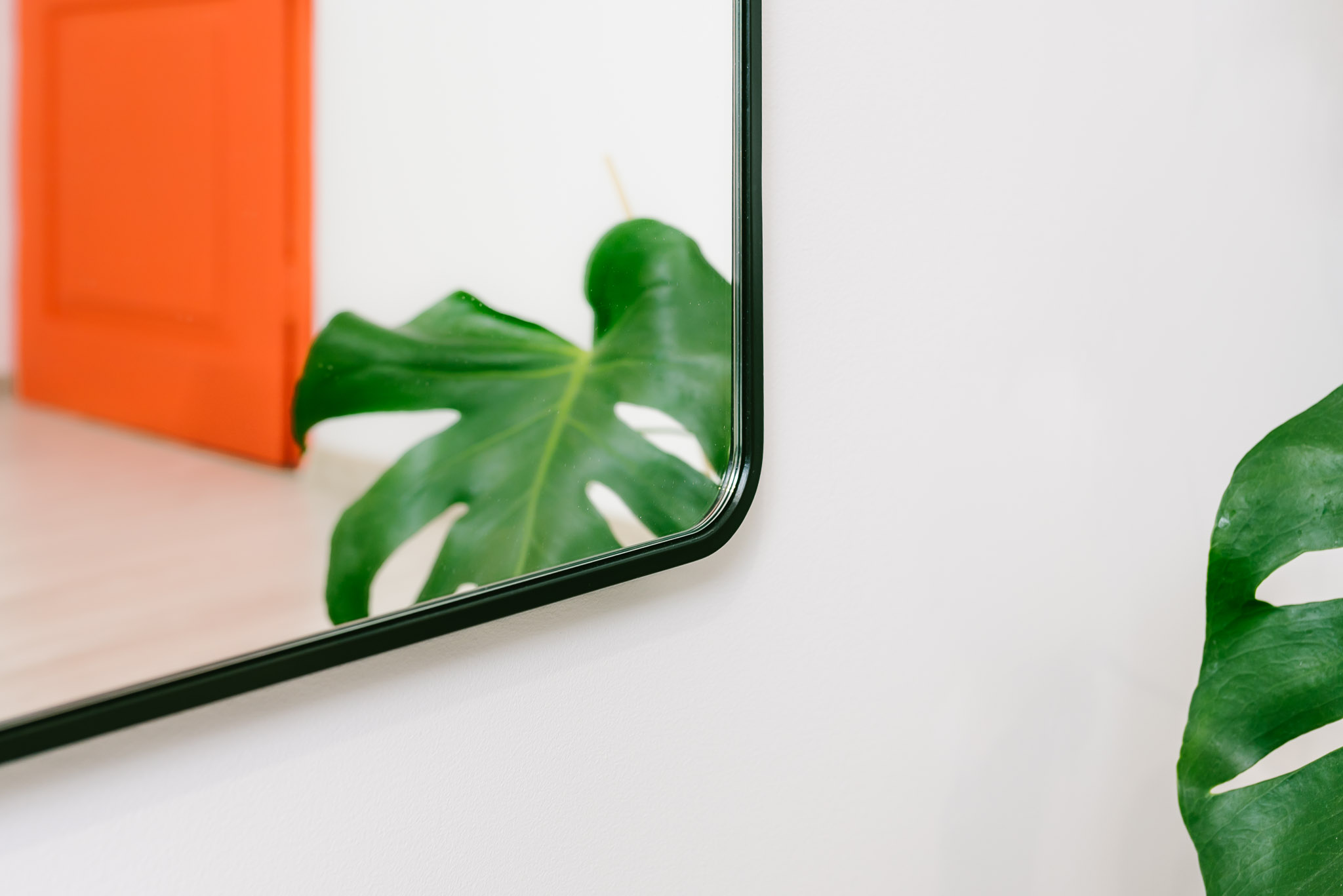 ZBLIŻENIE NA LUSTRO W CZARNEJ RAMIE Z ZAOKRĄGLONYMI NAROŻNIKAMI WISZĄCE W PRZEDPOKOJU