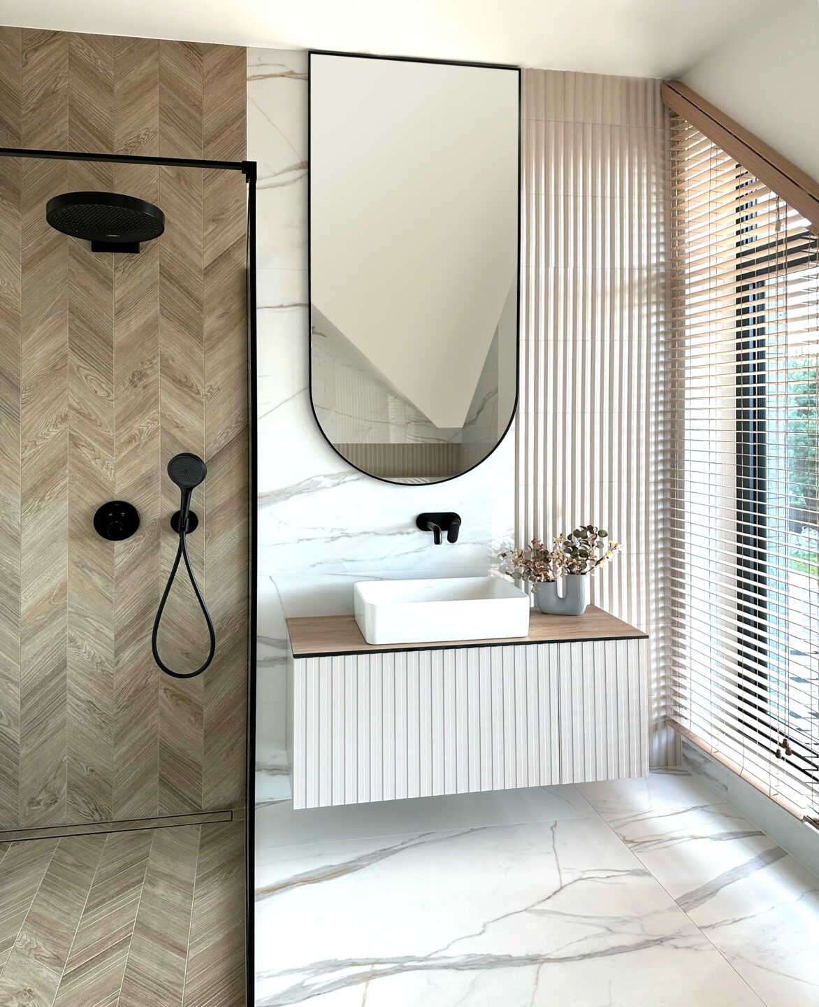 lustro arkadowe w czarnej ramie w łazience powieszone łukiem do dołu nad ryflowaną szafką