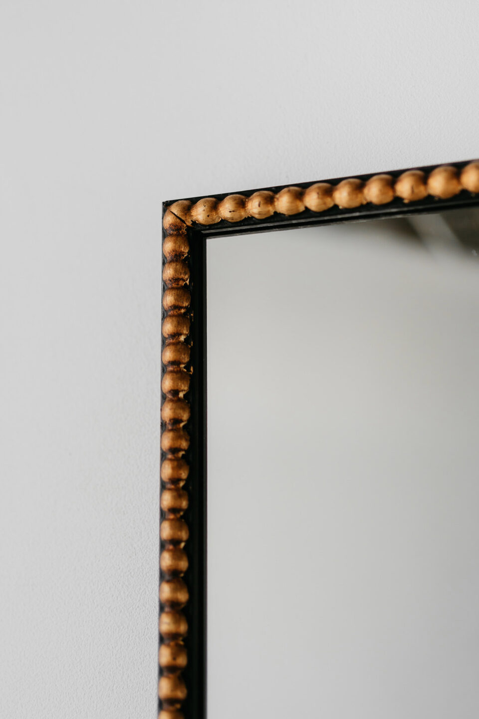 prostokatne lustro dots w kolorze wenge ze zlotymi kulkami na froncie ramy na bialej scianie