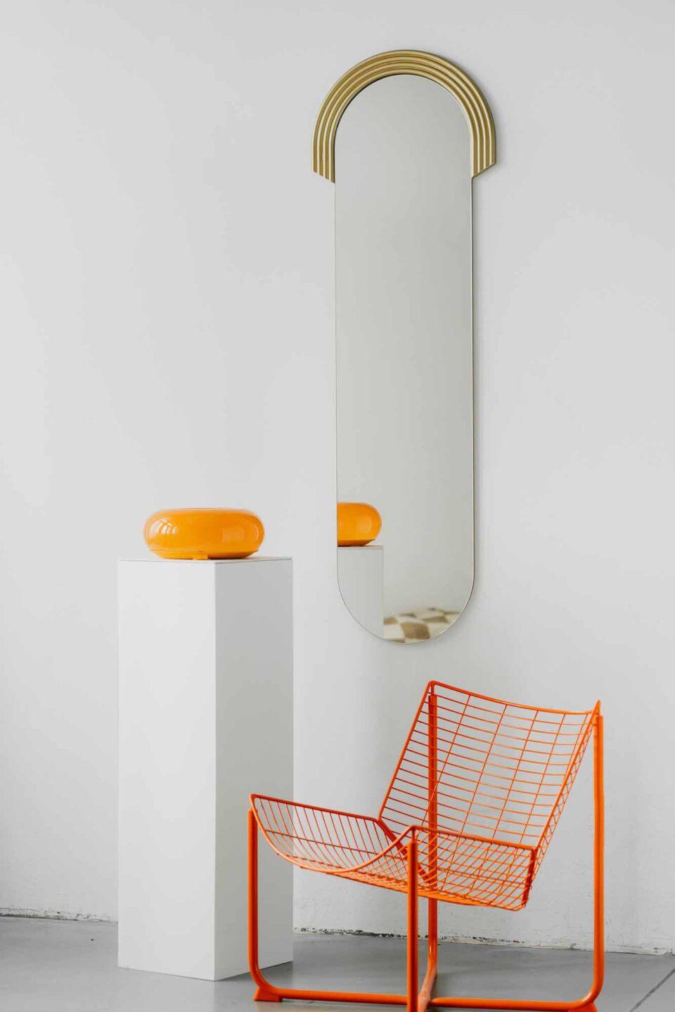 lustro owalne w formie kapsulki ze zlotym ryflowanym dekorem na gorze lustra powieszone na bialej scianie