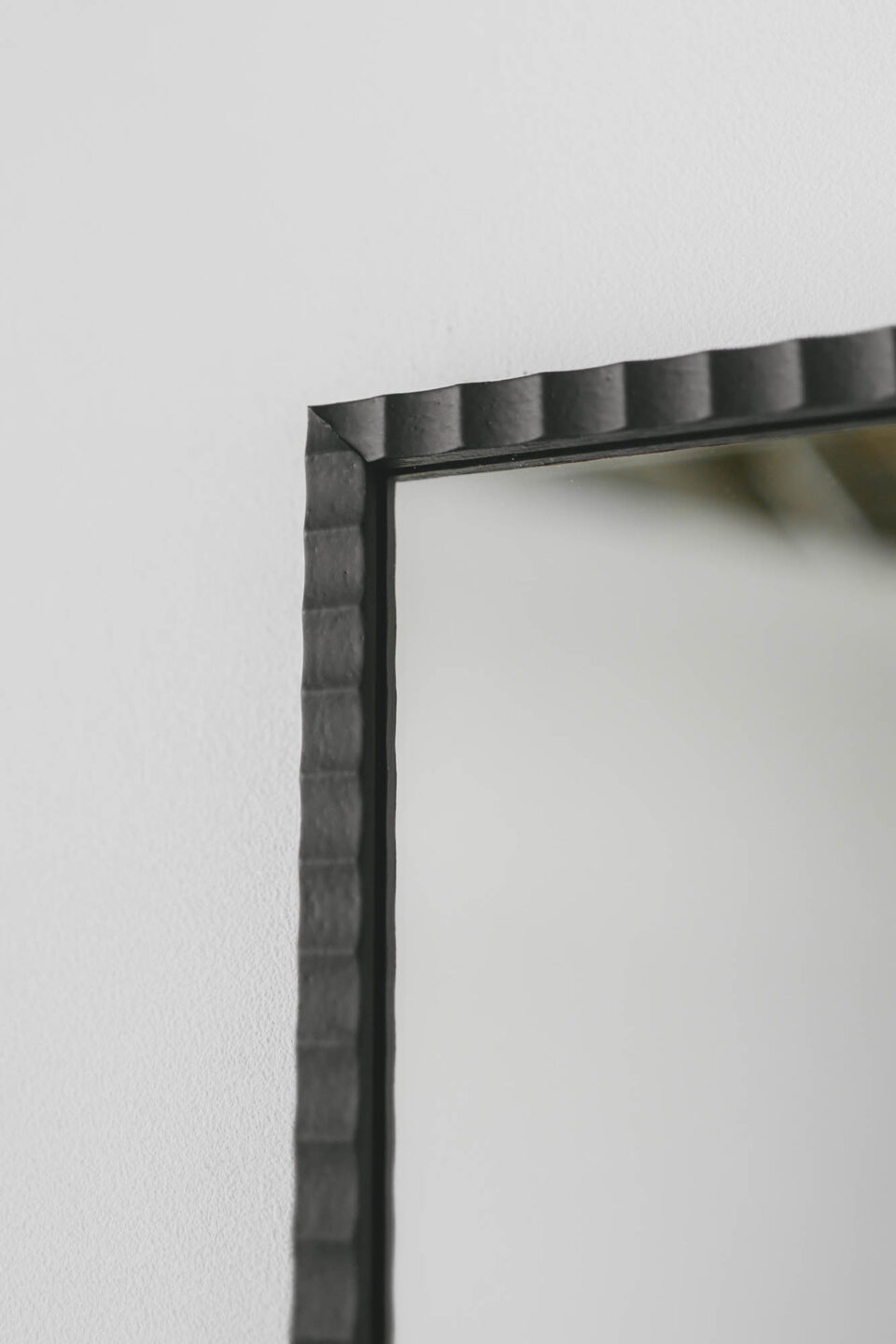 prostokatne lustro w czarnej pofalowanej waskiej ramie na bialej scianie