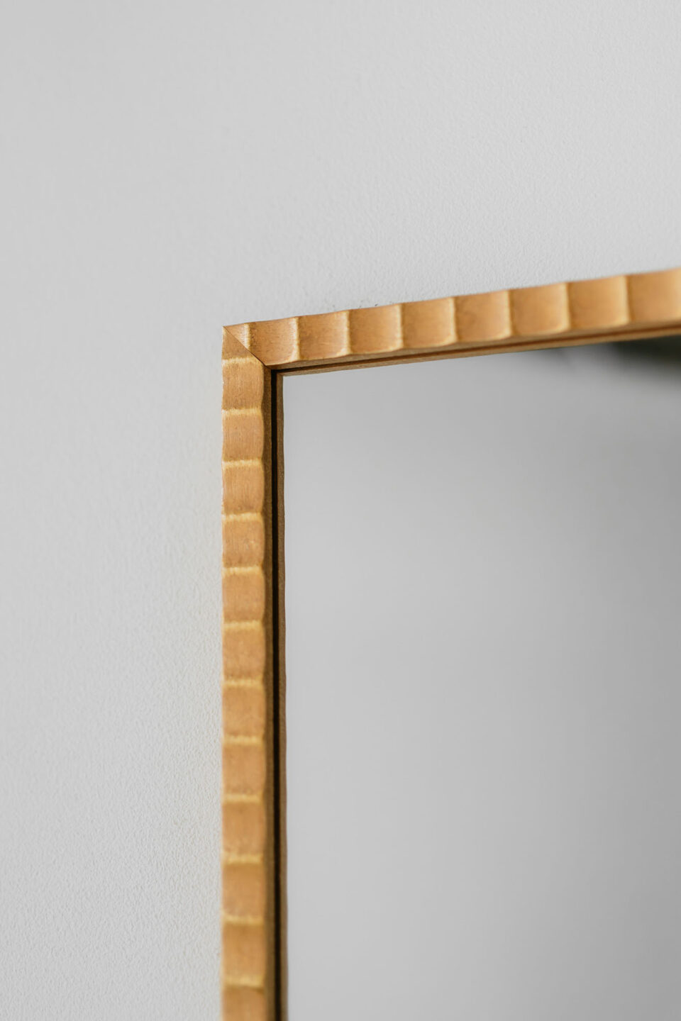 prostokatne lustro w zlotej pofalowanej ramie na bialej scianie