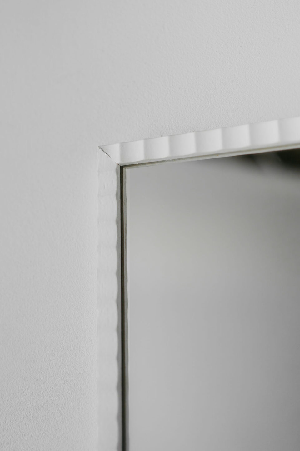 prostokatne lustro w pofalowanej waskiej bialej ramie na bialej scianie