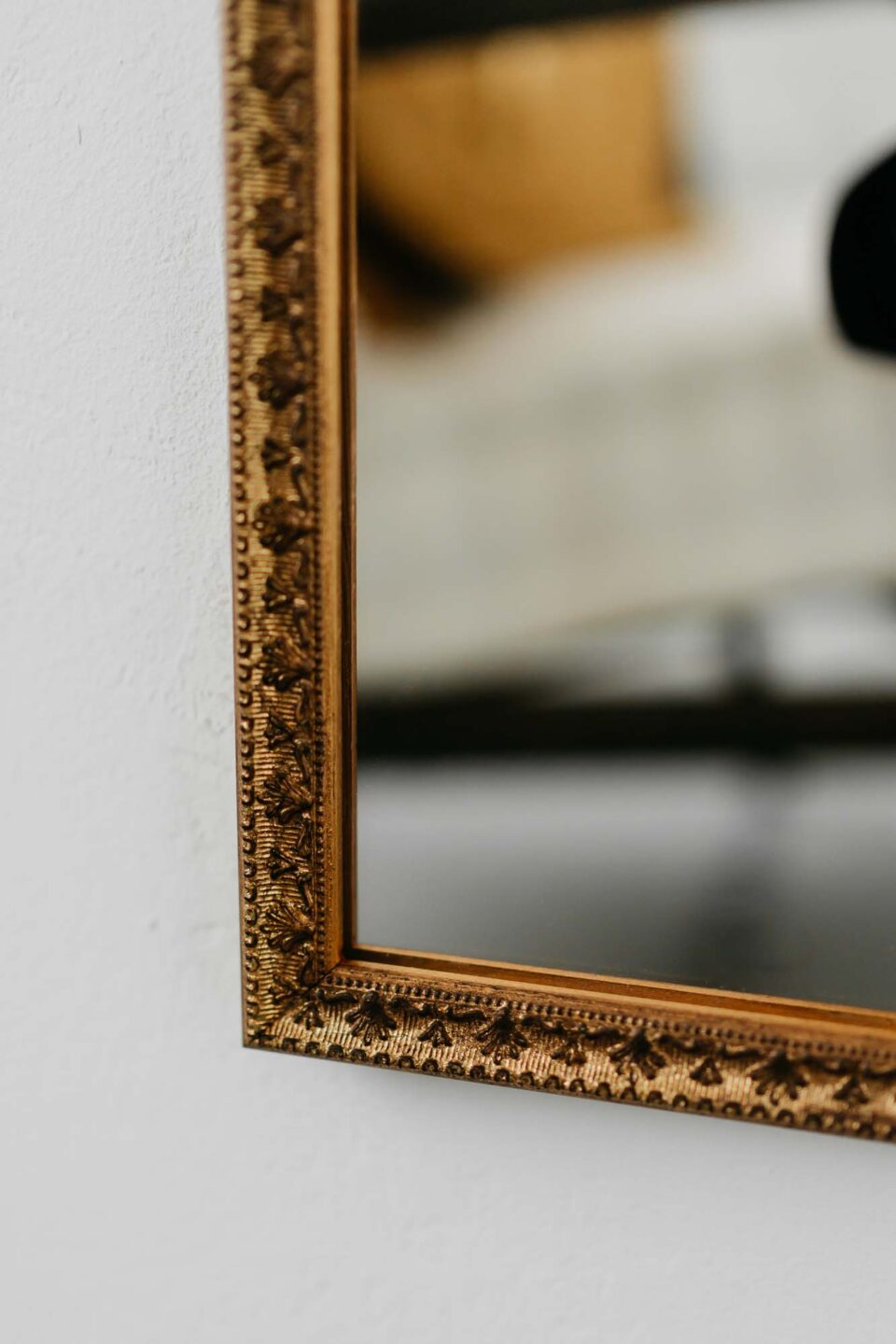 prostokatne lustro w waskiej ramie w kolorze starego zlota na bialej scianie
