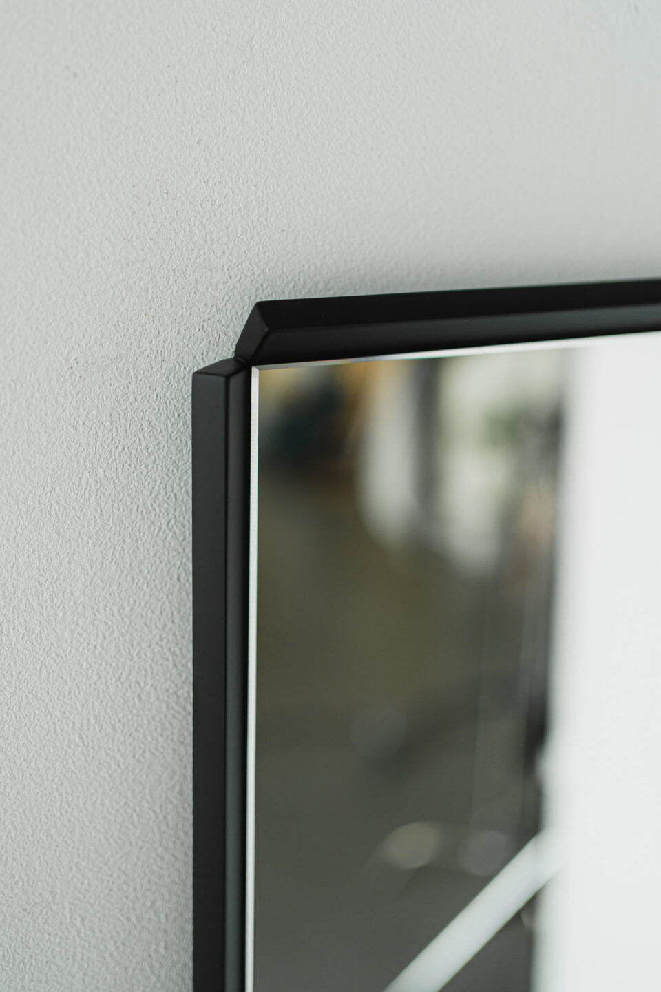 detal lustra oblique long w czarnej ramie na bialej scianie